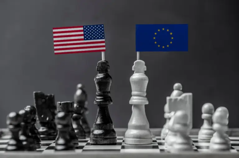 Due re degli scacchi, uno nero e uno bianco, con bandierine di USA e Unione Europea, contrapposti su una scacchiera